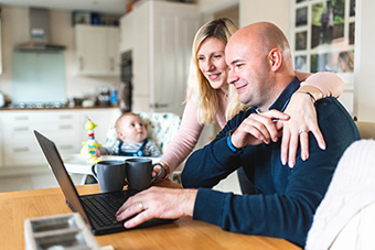 Couple on computer with baby in the background